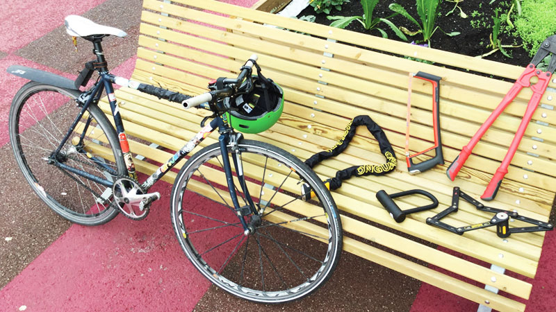 bici chiusa con catena e lucchetto appoggiata a una panchina